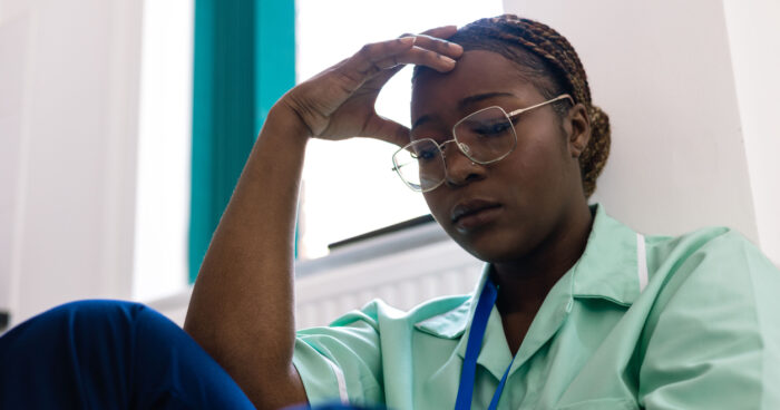 Healthcare professional sitting on the floor with hand on forehead, appearing tired and overwhelmed