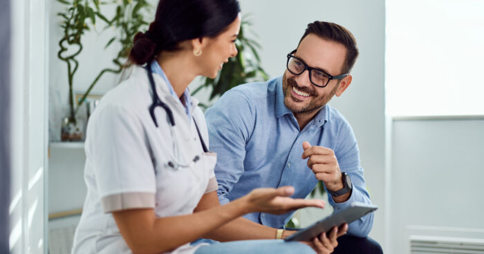 Female doctor discussing treatment plan with smiling male patient using tablet