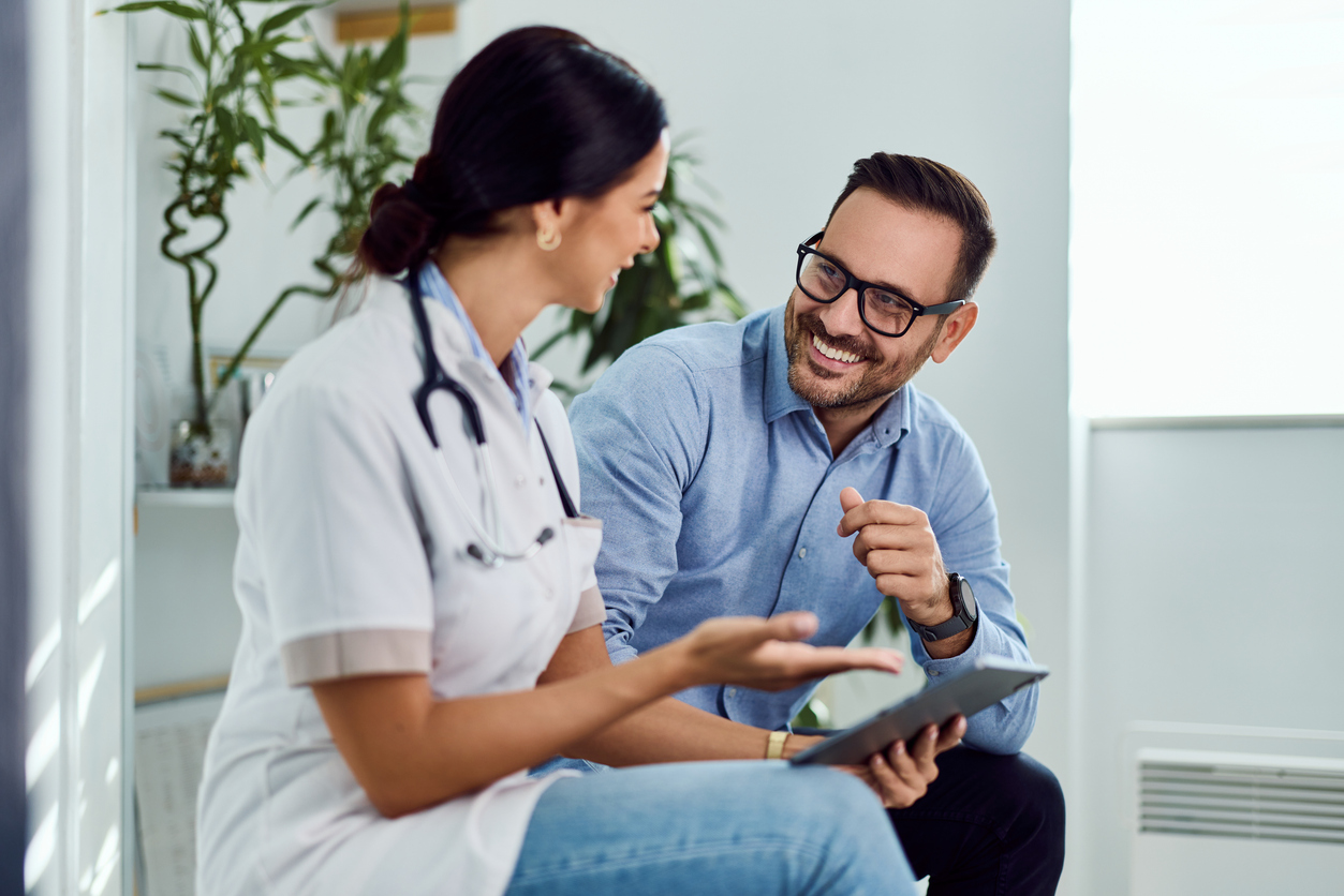 Female doctor discussing treatment plan with smiling male patient using tablet