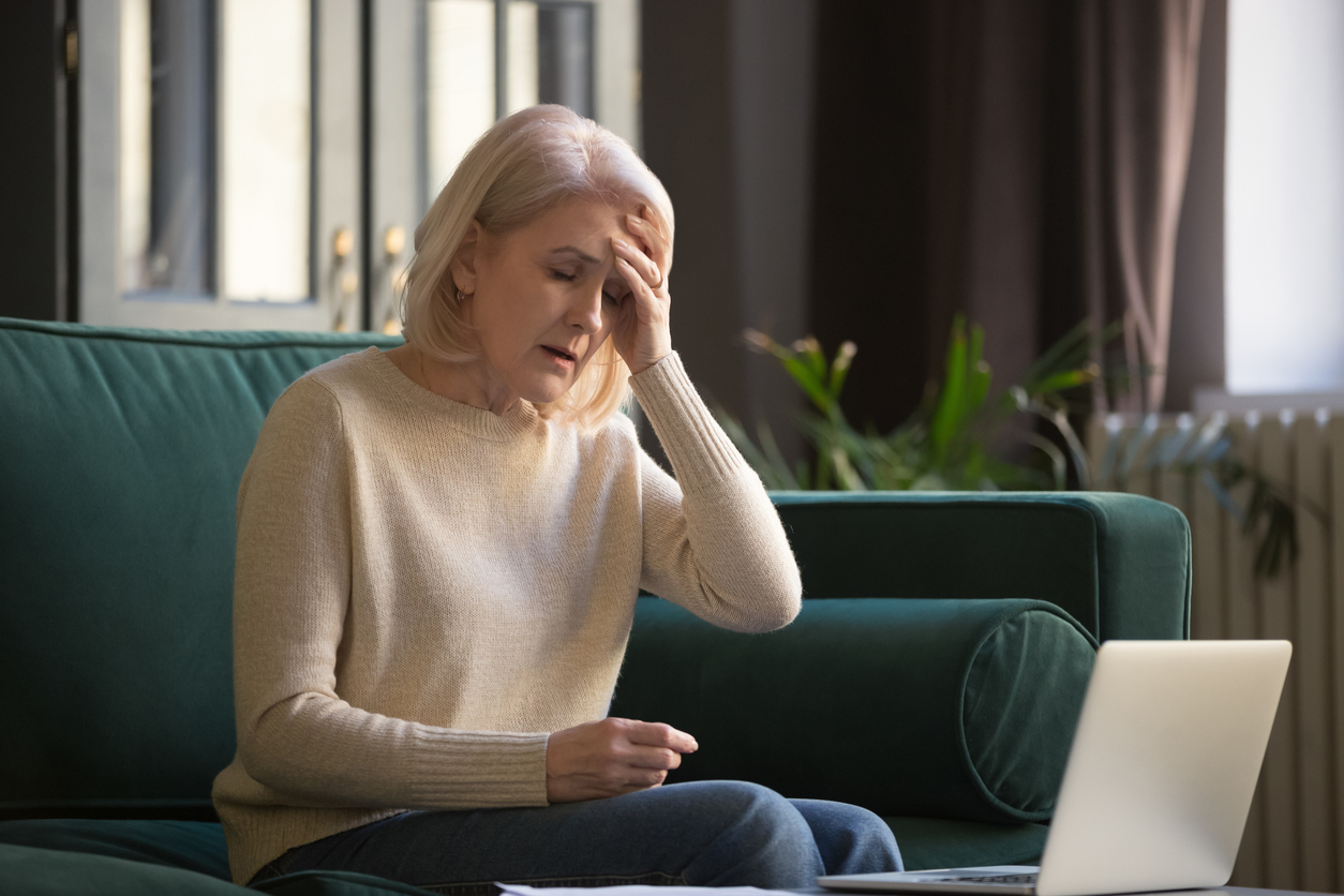 Tired stressed upset middle aged mature woman feeling sick headache after computer work sit at home on sofa, sad fatigued old senior lady grandmother touching head suffering from ache pain migraine